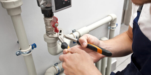 The man is installing the heater system in the house and checking pipes by the wrench